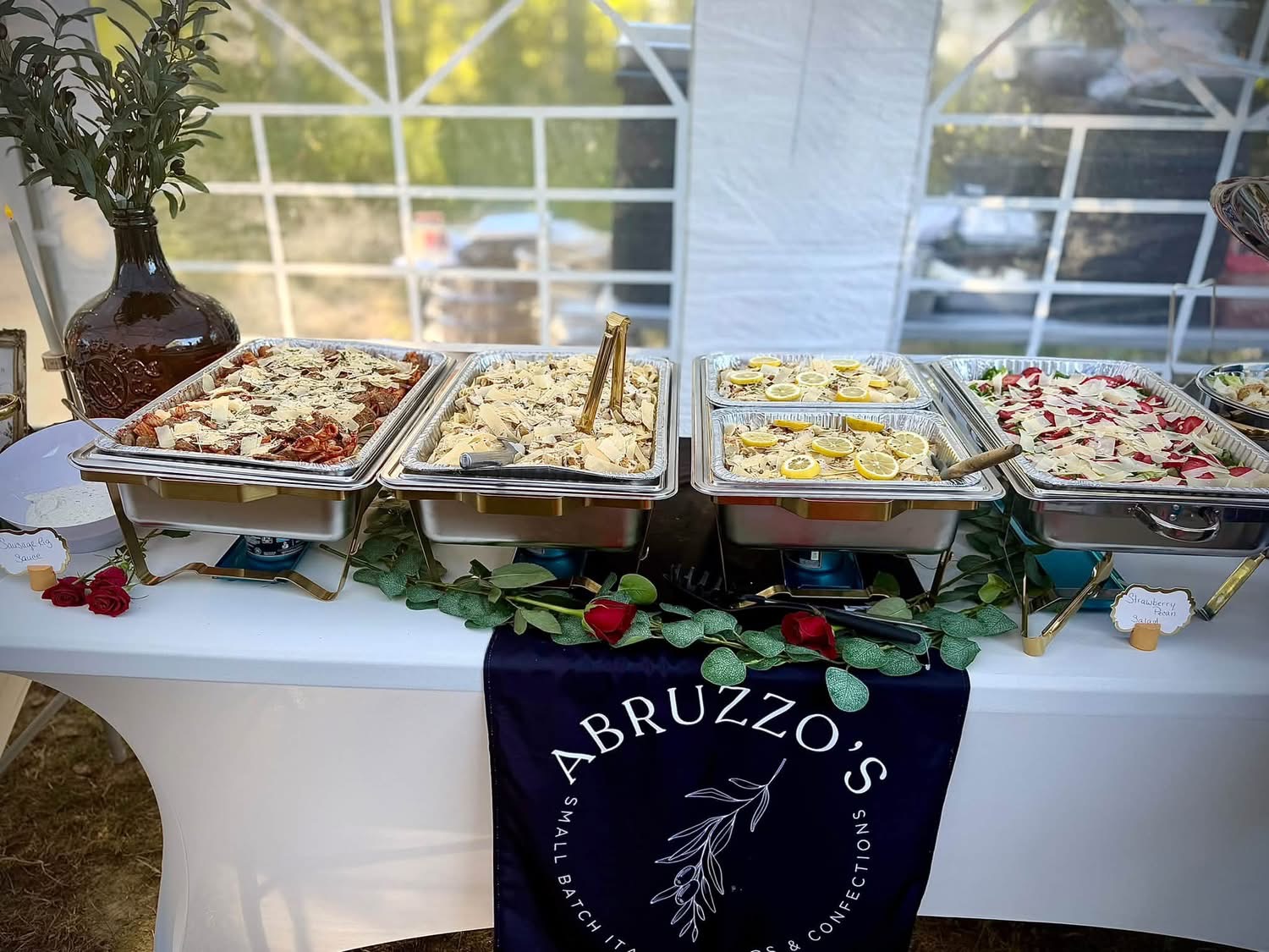 A catered Italian buffet with hot pasta dishes, strawberry pecan salad and floral décor