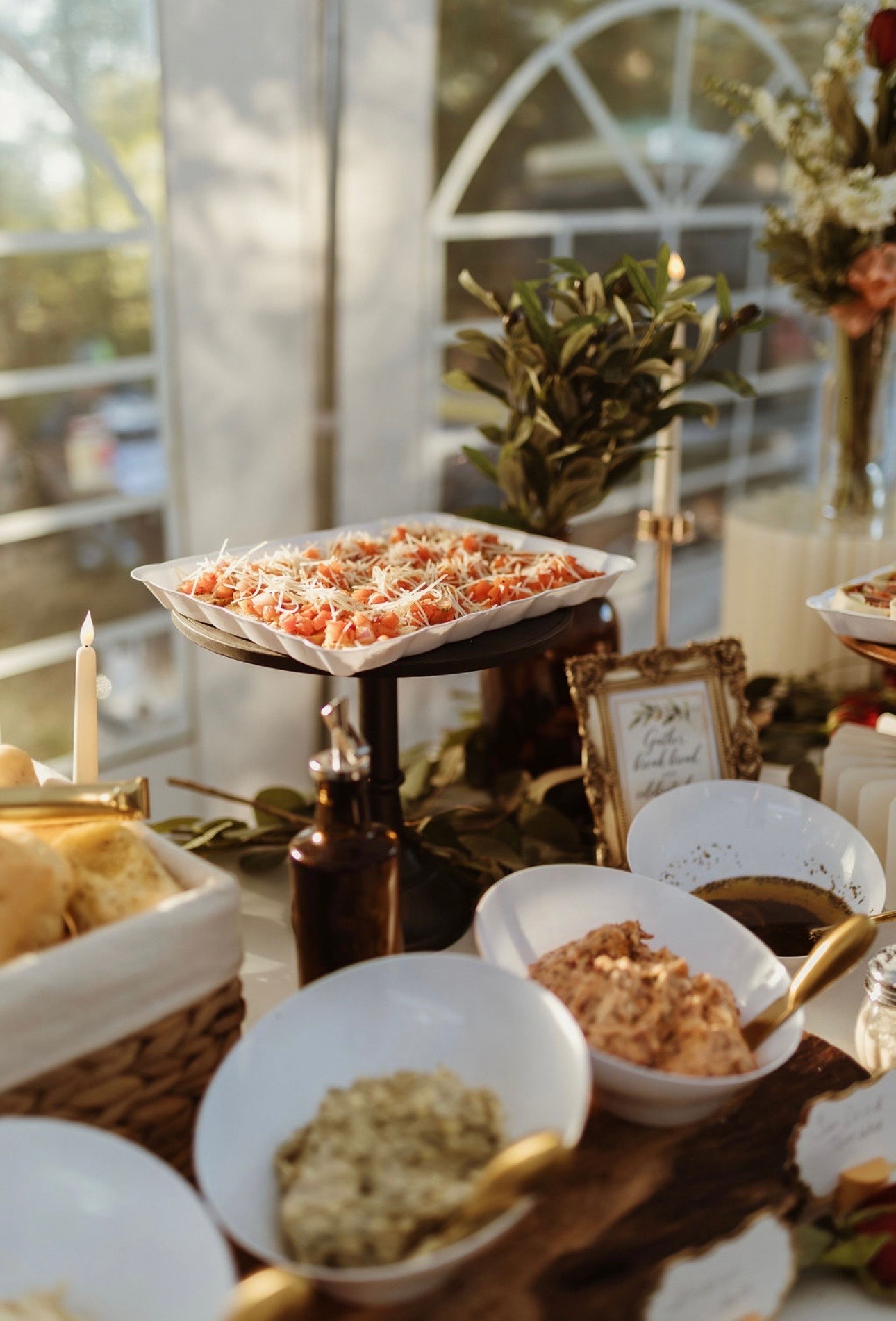 Bruschetta on a raised platter beside bowls of dips, a basket of rolls and taper candles