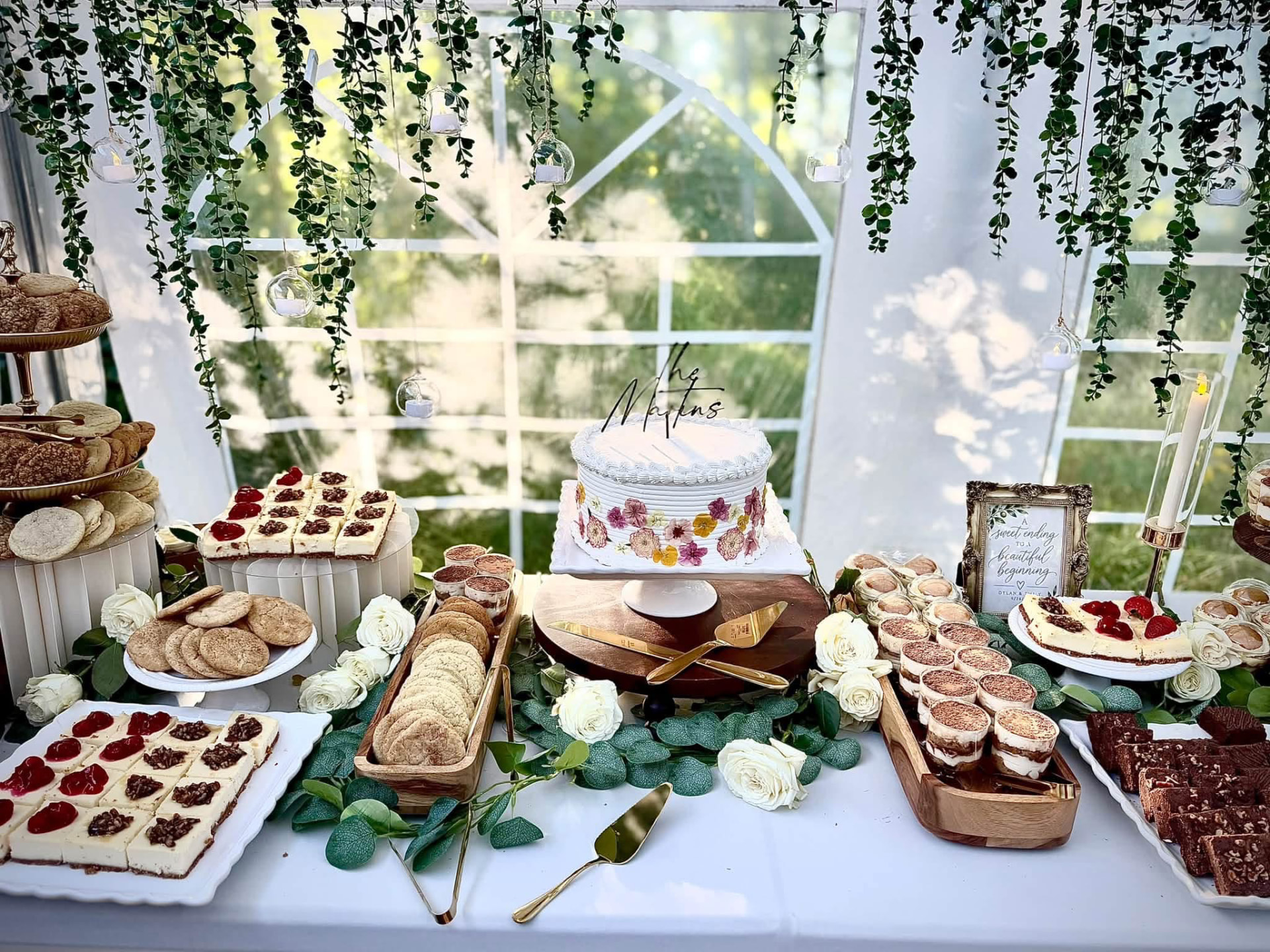 A wedding dessert table with a flower-decorated cake, cheesecakes, cookies and tiramisu cups